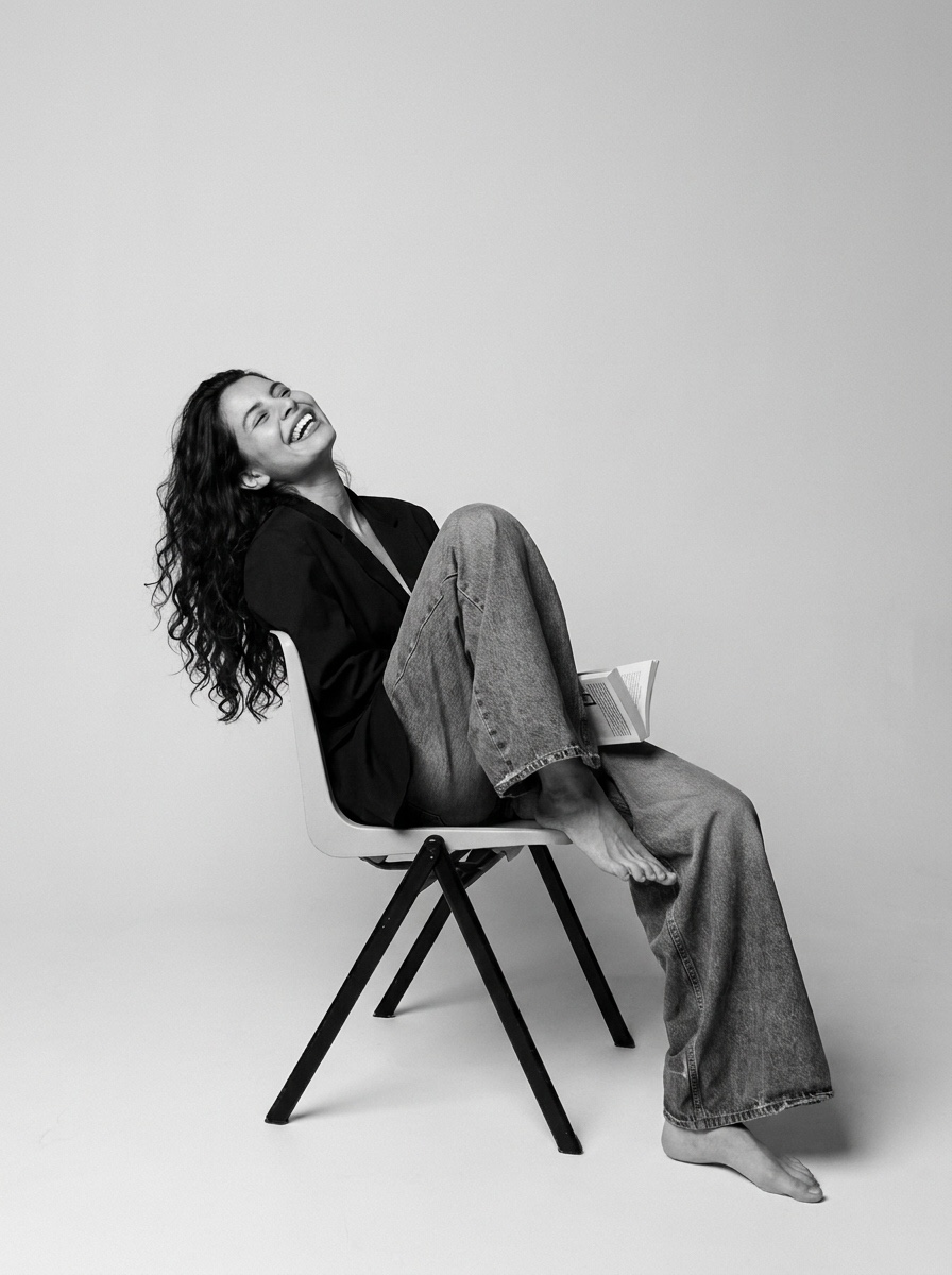 Nina Brenes sonriendo, sentada en una silla con un libro